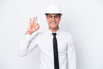 Young architect caucasian man with helmet and holding blueprints isolated on white background showing ok sign with fingers