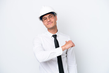 Young architect caucasian man with helmet and holding blueprints isolated on white background proud and self-satisfied