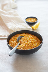 Yellow lentils and spoon in a black ceramic bowl on bright background. Lentil soup with fresh slice of lemon.  Minimal kitchen scene.