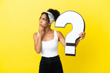 Young african american woman isolated on yellow background holding a question mark icon and having doubts
