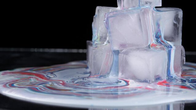 Multi-colored paint spreads over the surface of the ice cubes and flows down onto the plane.