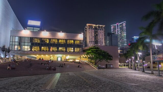 People sitting on the stairs near Hong Kong Cultural Centre with palms and towers on background timelapse hyperlapse.