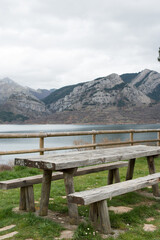 Fototapeta premium Picnic area with wooden table and bench. Magnificent view of the water reservoir at Caldas de Luna and the mountains around. Spain