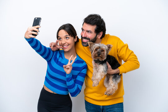 Young hispanic woman holding a dog isolated on white background making a selfie with the mobile