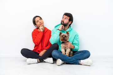 Young caucasian couple sitting on the floor with their pet isolated on white background standing...