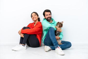 Fototapeta na wymiar Young caucasian couple sitting on the floor with their pet isolated on white background keeping arms crossed