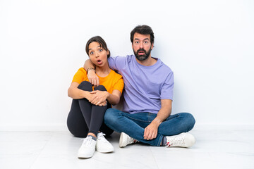 Fototapeta na wymiar Young caucasian couple sitting on the floor isolated on white background with surprise facial expression
