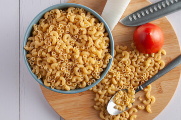 Raw or uncooked Elbow Pasta in a blue bowl and on woodenchooping board.