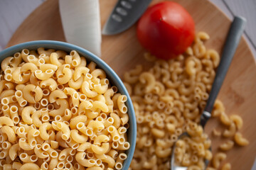 Raw or uncooked Elbow Pasta in a blue bowl and on woodenchooping board.