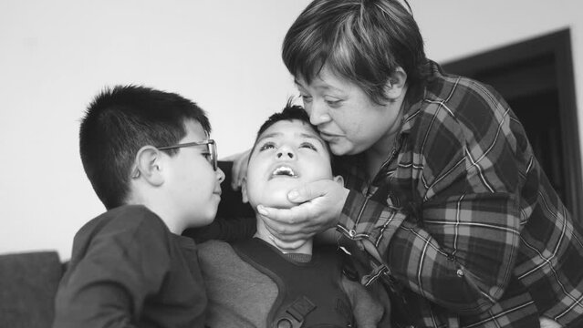 Mother having tender moment with sons at home - Boy kissing brother with disability on wheelchair