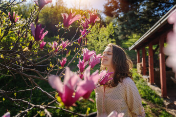 Young beautiful woman enjoying the spring of her home in the garden near a blooming magnolia tree inhaling the aroma of flowers - Powered by Adobe