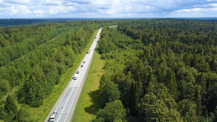 Fototapeta na wymiar A wonderful green road from a helicopter . Clip. A long paved road with cars and a huge green summer forest around.