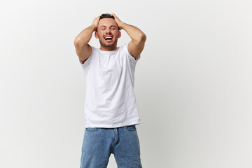 Fototapeta premium Overjoyed screaming angry tanned handsome man in basic t-shirt tearing his hair out posing isolated on over white studio background. Copy space Banner Mockup. People emotions Lifestyle concept