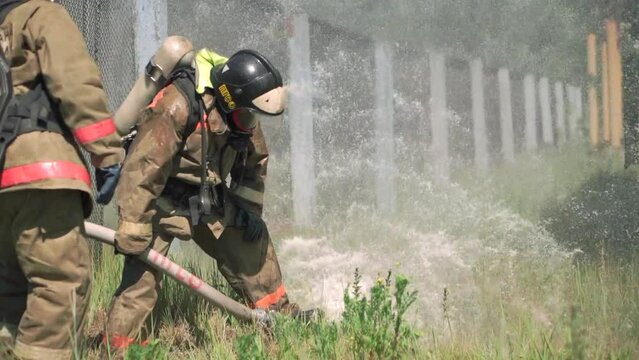 Firefighters. Clip. Two masked men who conduct exercises with a hose and water with special equipment and in a special uniform.