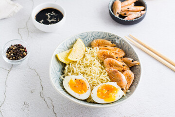 Chinese noodles with fried shrimp, boiled egg and lemon in a bowl on the table. Close-up