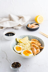 Chinese noodles with fried shrimp, boiled egg and lemon in a bowl on the table. Vertical view