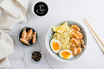 Chinese noodles with fried shrimp, boiled egg and lemon in a bowl on the table. Top view