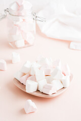 White and pink heart-shaped marshmallows on a saucer on a pink background. Vertical view