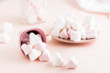 White and pink heart-shaped marshmallows are scattered from a cup