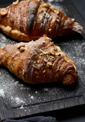 baked croissants on a black wooden board sprinkled with powdered sugar