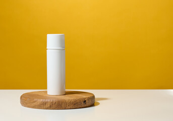 white plastic round tube for cosmetics, creams and liquid gels on a wooden podium, yellow background