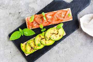 Appetizing sandwiches with avocado and tomatoes on grain bread on slate. Top view
