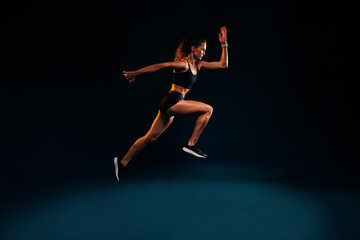Obraz na płótnie Canvas Fit woman running and jumping in the studio. Young female sprinting against dark background.