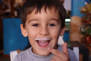 Dark-haired 4-year-old boy smiling and showing milk-stained face.