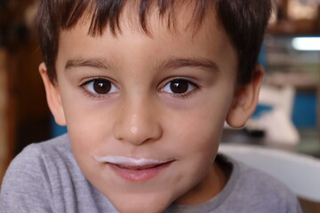 Portrait of brown-eyed brunette boy with milk foam mustache on upper lip.