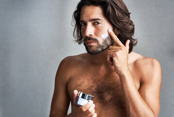 Real men moisturize. Studio shot of a handsome young man applying moisturiser to his face against a...