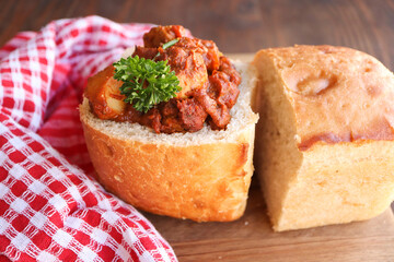 Bunny chow filled with chicken curry. A traditional South African cuisine called a bunny chow filled with chicken curry. A hollowed out loaf of bread filled with chicken curry 