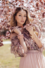 beautiful woman with blond curly hair in elegant dress posing in spring flowering park with...