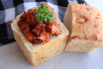 A bunny chow filled with chicken curry. A traditional South African cuisine called a bunny chow filled with chicken curry. Hollowed out loaf of bread filled with chicken curry 