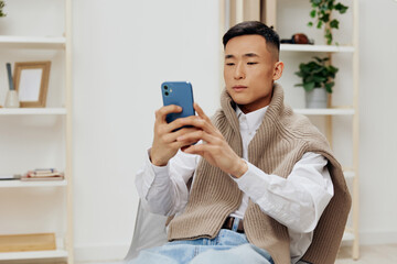 Asian man communication with the phone in his hands sits on a chair interior