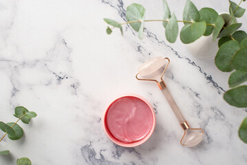 Top view photo of eucalyptus rose quartz roller and pink eye patches on white marble background with copyspace