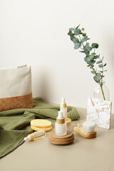 Natural SPA cosmetic products set with eucalyptus leaves and green towel on table in bathroom. Wooden and glass beauty product bottles, body brush, cosmetic discs.