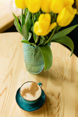 cup of coffee on the table with yellow tulips on the background