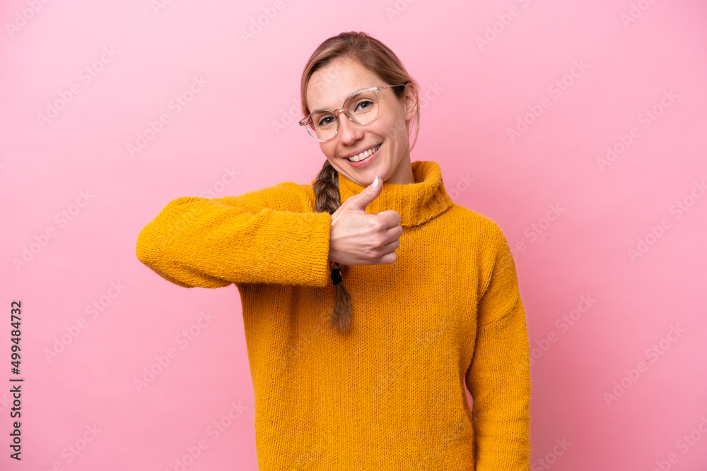 Wall mural Young caucasian woman isolated on pink background giving a thumbs up gesture