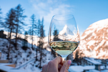 Tourist holding wineglass with view of Matterhorn and snowy town against blue sky. Beautiful Zermatt