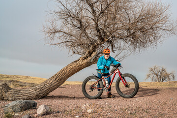 Obraz premium senior male cyclist with a fat mountain bike in northern Colorado prairie, early spring scenery in Soapstone Prairie Natural Area near Fort Collins