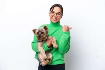 Young hispanic woman holding a dog isolated on white background pointing to the side to present a product