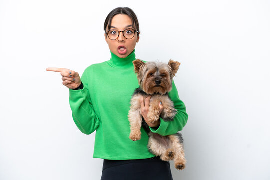 Young hispanic woman holding a dog isolated on white background surprised and pointing side