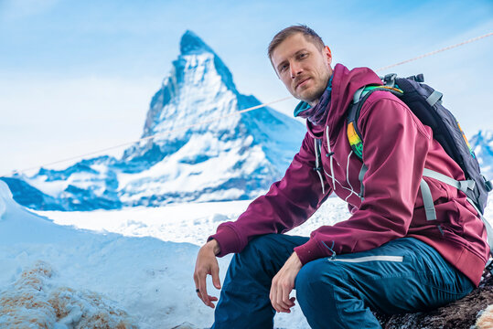Portrait of young tourist sitting on rock against Matterhorn mountain in winter
