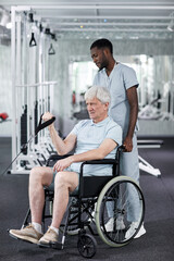 Fototapeta na wymiar Full length portrait of senior man using wheelchair in gym during rehabilitation therapy at clinic