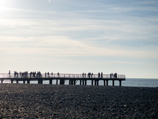 Silhouettes of people on the bridge on the seashore. People see off the sunset. Sea coast. Pier on the sea.