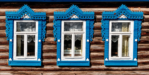 Old wooden windows with carved architraves. Log facade of typical rural Russian house. - obrazy, fototapety, plakaty