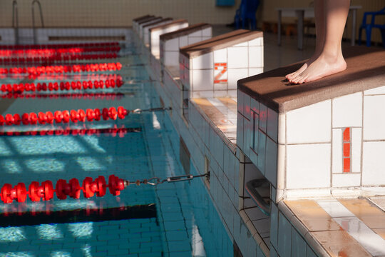 Starting blocks with dividing tracks in the pool. The edge of the room is a sports pool. The child stands on the starting block with the number 1