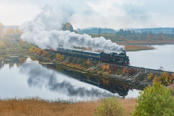 Fototapeta na wymiar Retro steam train moves along the lake at autumn morning.