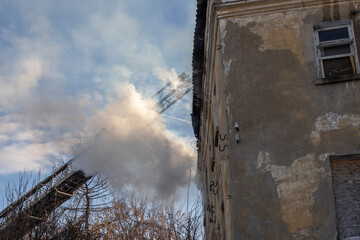 Firefighter works on boom of fire engine. Fireman on sky background. Burning old building in the historic center..Rescuers on a retractable ladder in the smoke.