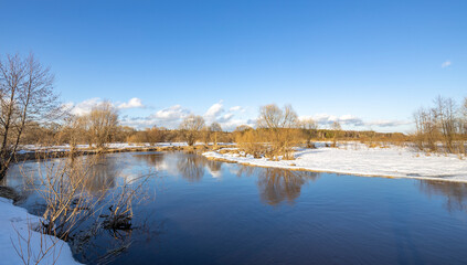 March sunny day by the river. A picturesque landscape, early spring, a river with snow-covered banks. The first thaws, the snow is melting.